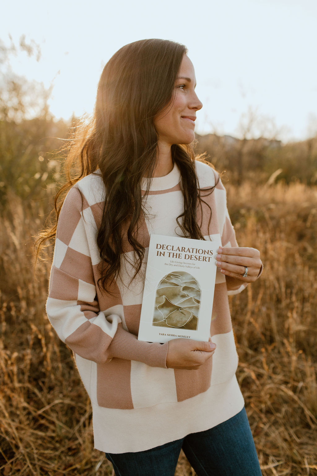 Tara Sierra Moseley in a golden field holding Declarations in the Desert